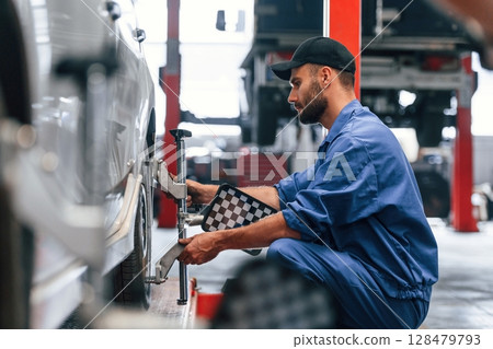 Sitting, checking the tire. Auto mechanic working in garage. Repair service 128479793