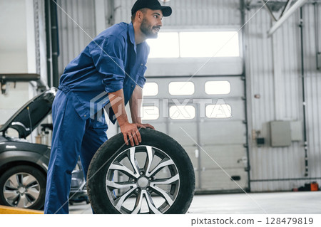 New tire, moving it. Auto mechanic working in garage. Repair service New tire, moving it. Auto mechanic working in garage. Repair service 128479819