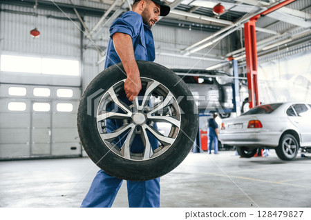 With brand new wheel. Auto mechanic working in garage. Repair service 128479827