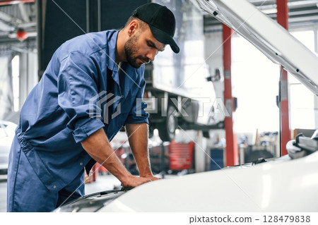 Working by repairing the car. Hood is opened. Auto mechanic is in garage. Repair service Working by repairing the car. Hood is opened. Auto mechanic is in garage. Repair service 128479838