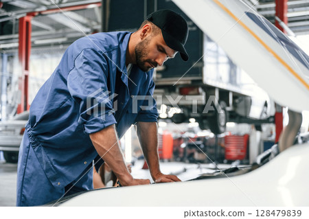 Working by repairing the car. Hood is opened. Auto mechanic is in garage. Repair service Working by repairing the car. Hood is opened. Auto mechanic is in garage. Repair service 128479839