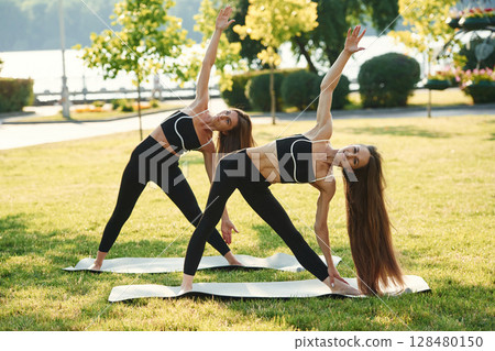 Doing yoga exercises. Two women in sport clothes are doing exercises outdoors on the field Doing yoga exercises. Two women in sport clothes are doing exercises outdoors on the field 128480150