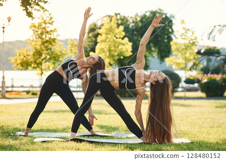 Doing yoga exercises. Two women in sport clothes are doing exercises outdoors on the field Doing yoga exercises. Two women in sport clothes are doing exercises outdoors on the field 128480152