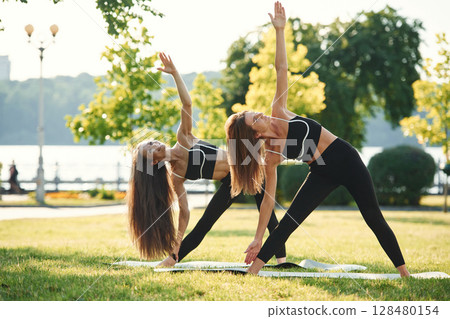 Doing yoga exercises. Two women in sport clothes are doing exercises outdoors on the field Doing yoga exercises. Two women in sport clothes are doing exercises outdoors on the field 128480154