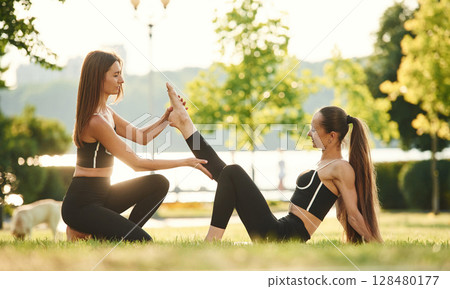 Teaching the new exercises. Two women in sport clothes are doing exercises outdoors on the field 128480177