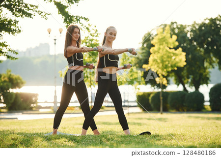 With dumbbells. Two women in sport clothes are doing exercises outdoors on the field With dumbbells. Two women in sport clothes are doing exercises outdoors on the field 128480186