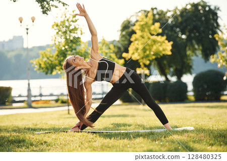 Hands and legs stretching. Beautiful young woman in sportive clothes is in the park at sunny daytime 128480325