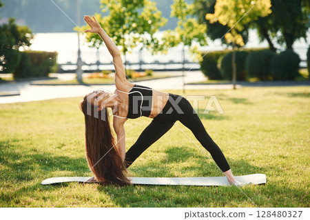 On the yoga mat. Beautiful young woman in sportive clothes is in the park at sunny daytime 128480327