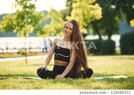 On the yoga mat. Beautiful young woman in sportive clothes is in the park at sunny daytime 128480331