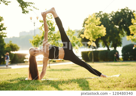 Exercises for flexibility. Beautiful young woman in sportive clothes is in the park at sunny daytime Exercises for flexibility. Beautiful young woman in sportive clothes is in the park at sunny daytime 128480340