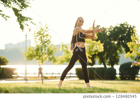 Warming up hands. Beautiful young woman in sportive clothes is in the park at sunny daytime Warming up hands. Beautiful young woman in sportive clothes is in the park at sunny daytime 128480345