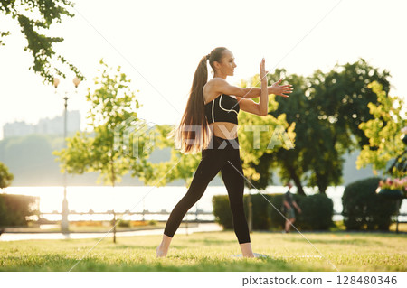 Warming up hands. Beautiful young woman in sportive clothes is in the park at sunny daytime Warming up hands. Beautiful young woman in sportive clothes is in the park at sunny daytime 128480346
