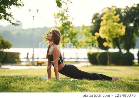 Exercises for the spine. Beautiful young woman in sportive clothes is in the park at sunny daytime Exercises for the spine. Beautiful young woman in sportive clothes is in the park at sunny daytime 128480376
