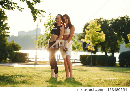 Standing and posing. Two women in sport clothes are doing exercises outdoors on the field Standing and posing. Two women in sport clothes are doing exercises outdoors on the field 128480564