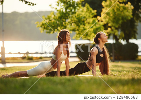 Conception of sport. Two women are doing exercises outdoors on the field Conception of sport. Two women are doing exercises outdoors on the field 128480568