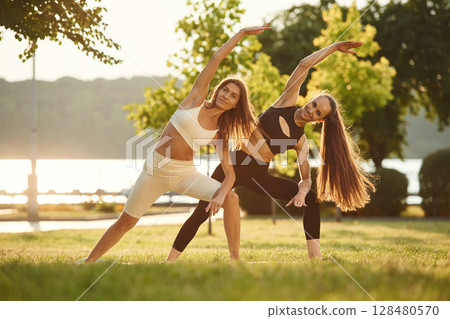 Conception of sport. Two women are doing exercises outdoors on the field Conception of sport. Two women are doing exercises outdoors on the field 128480570