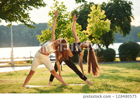 Two women in sport clothes are doing exercises outdoors on the field Two women in sport clothes are doing exercises outdoors on the field 128480575