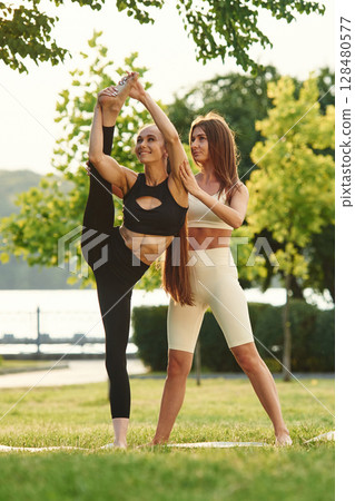 Two women in sport clothes are doing exercises outdoors on the field Two women in sport clothes are doing exercises outdoors on the field 128480577