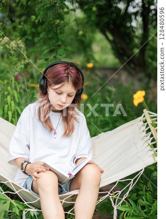 Teenage girl reading and listening to music in hammock outdoors Teenage girl reading and listening to music in hammock outdoors 128480596