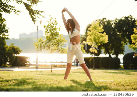 White sportive clothes. Beautiful young woman is in the park at sunny daytime 128480629