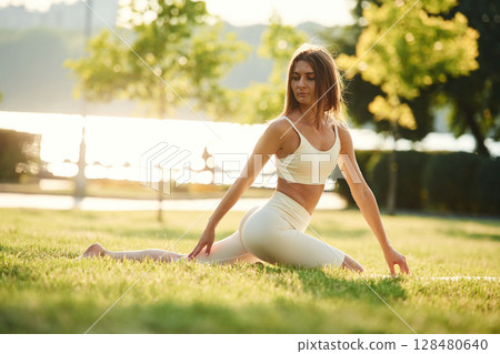 Sits on the splits. Beautiful young woman in sportive clothes is in the park at sunny daytime Sits on the splits. Beautiful young woman in sportive clothes is in the park at sunny daytime 128480640
