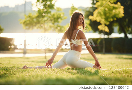Sits on the splits. Beautiful young woman in sportive clothes is in the park at sunny daytime 128480642