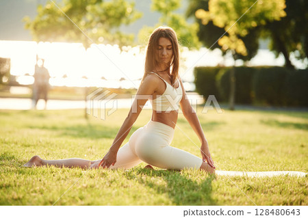 Sits on the splits. Beautiful young woman in sportive clothes is in the park at sunny daytime Sits on the splits. Beautiful young woman in sportive clothes is in the park at sunny daytime 128480643