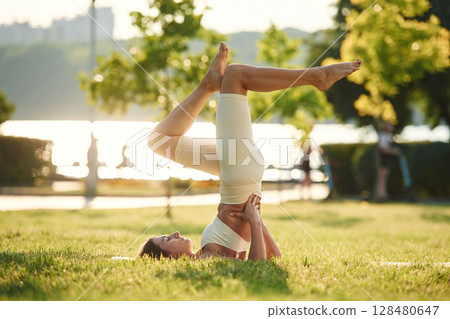 With legs up. Beautiful young woman in sportive clothes is in the park at sunny daytime 128480647