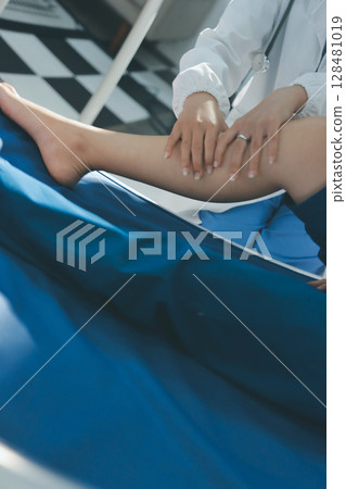 Female doctor hands doing physical therapy By extending the leg and knee of a male patient 128481019