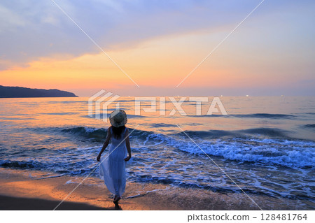 Woman walking on the beach at sunset 128481764