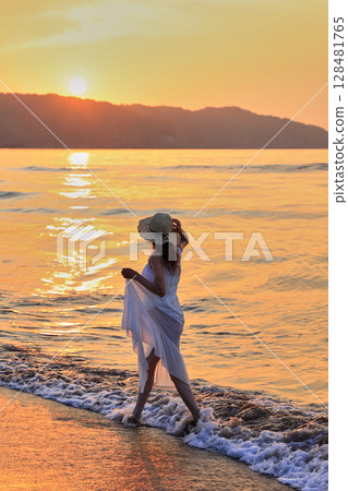 Woman walking on the beach at sunset 128481765