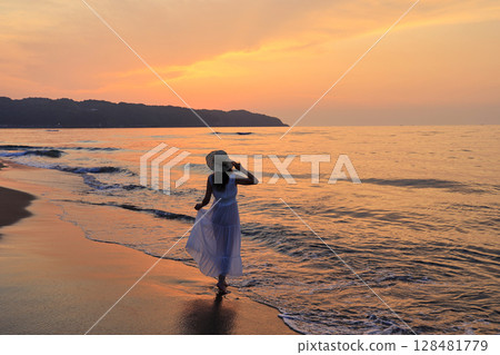 Woman walking on the beach at sunset 128481779