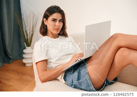 On the sofa with laptop. Beautiful woman in casual clothes is at home in domestic room On the sofa with laptop. Beautiful woman in casual clothes is at home in domestic room 128482575