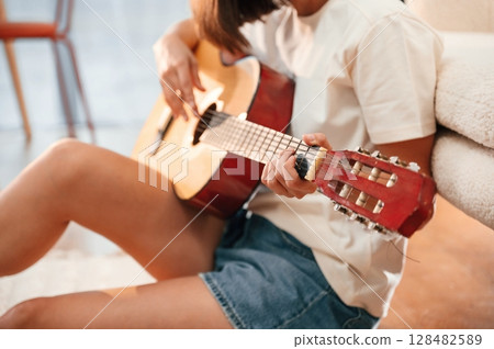 With classical guitar in hands. Beautiful woman in casual clothes is at home in domestic room With classical guitar in hands. Beautiful woman in casual clothes is at home in domestic room 128482589
