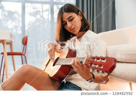 Learning to play classical guitar. Beautiful woman in casual clothes is at home in domestic room Learning to play classical guitar. Beautiful woman in casual clothes is at home in domestic room 128482592