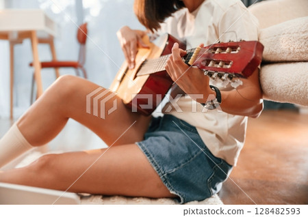 Learning to play classical guitar. Beautiful woman in casual clothes is at home in domestic room 128482593