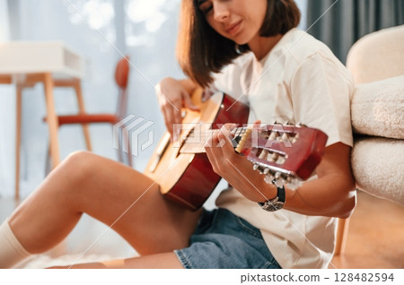 Learning to play classical guitar. Beautiful woman in casual clothes is at home in domestic room Learning to play classical guitar. Beautiful woman in casual clothes is at home in domestic room 128482594