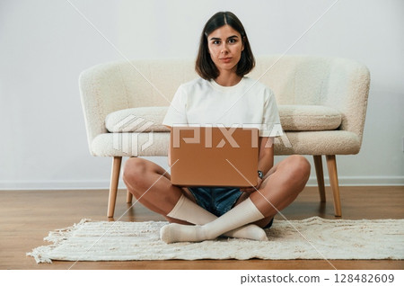 Sitting on the floor and using laptop. Beautiful woman in casual clothes is at home in domestic room 128482609