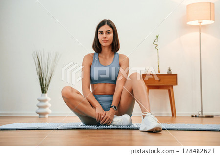 On yoga mat. Pretty woman in sportive clothes have fitness day indoors 128482621