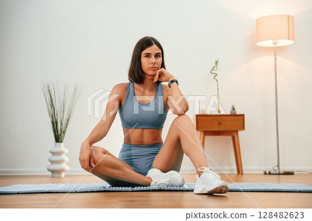 On yoga mat. Pretty woman in sportive clothes have fitness day indoors 128482623
