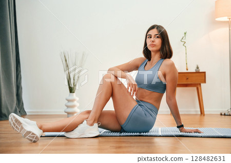 On yoga mat. Pretty woman in sportive clothes have fitness day indoors 128482631