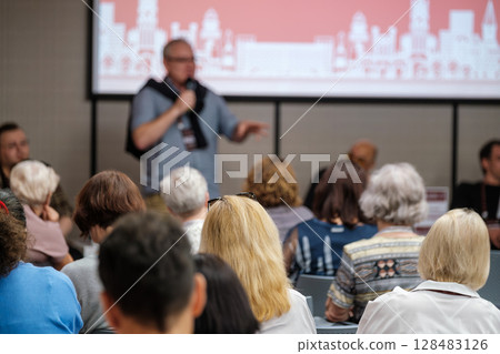 Speaker addressing audience in conference room with presentation screen Speaker addressing audience in conference room with presentation screen 128483126