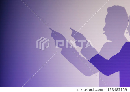 Silhouettes of a speaker on stage holding objects with a purple background 128483139