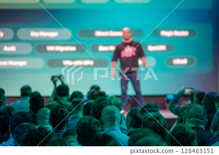 Speaker presenting at conference with audience in focus and blurred speaker Speaker presenting at conference with audience in focus and blurred speaker 128483151