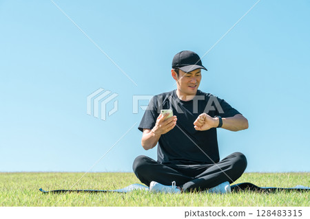 Middle-aged man in sportswear doing yoga, stretching and health care using smart watch and smart band Middle-aged man in sportswear doing yoga, stretching and health care using smart watch and smart band 128483315