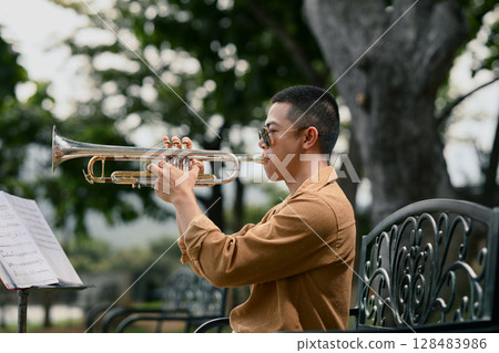 Trumpet player in sunglasses rehearsing outdoors with music stand Trumpet player in sunglasses rehearsing outdoors with music stand 128483986