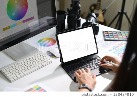 Photographer working on digital tablet with color charts and editing tools on desk 128484010