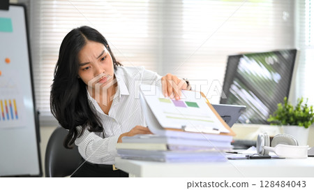 Overwhelmed office worker dealing with paperwork stress during a busy workday 128484043