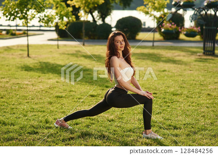 Exercises in the park at sunny daytime. Beautiful young woman in sportive clothes Exercises in the park at sunny daytime. Beautiful young woman in sportive clothes 128484256