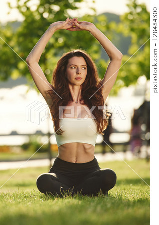 Yoga practice. Beautiful young woman in sportive clothes is in the park at sunny daytime Yoga practice. Beautiful young woman in sportive clothes is in the park at sunny daytime 128484300